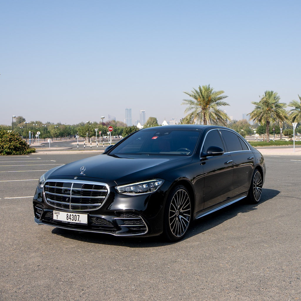 Black Mercedes S580 luxury sedan parked on an open road with a cityscape in the background.
